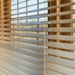 A set of vinyl blinds hung up against a large bright window.