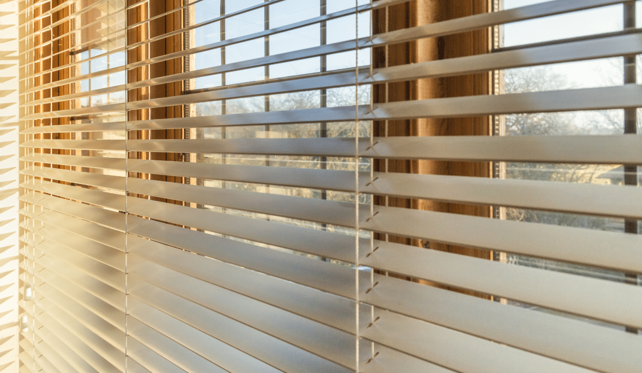 A set of vinyl blinds hung up against a large bright window.