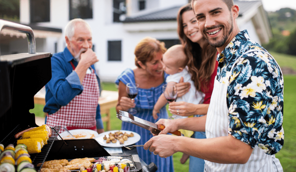 A family standing around a BBQ grill, with two men wearing BBQ aprons.