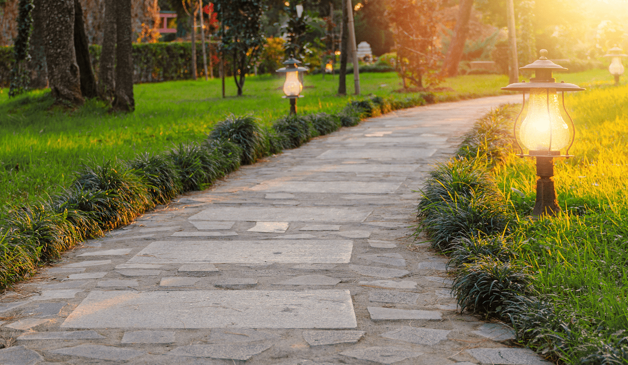 A front garden path with grass on either side and small lit lamps.