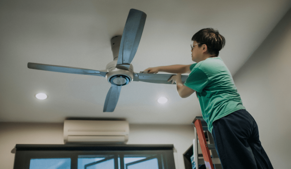 A person installing a smart ceiling fan inside a home.