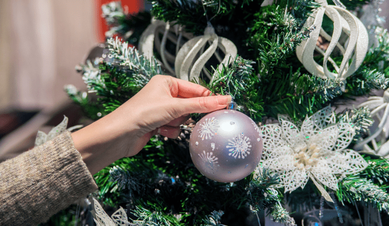 A person hand in view putting a bauble up onto a green artificial Christmas tree.